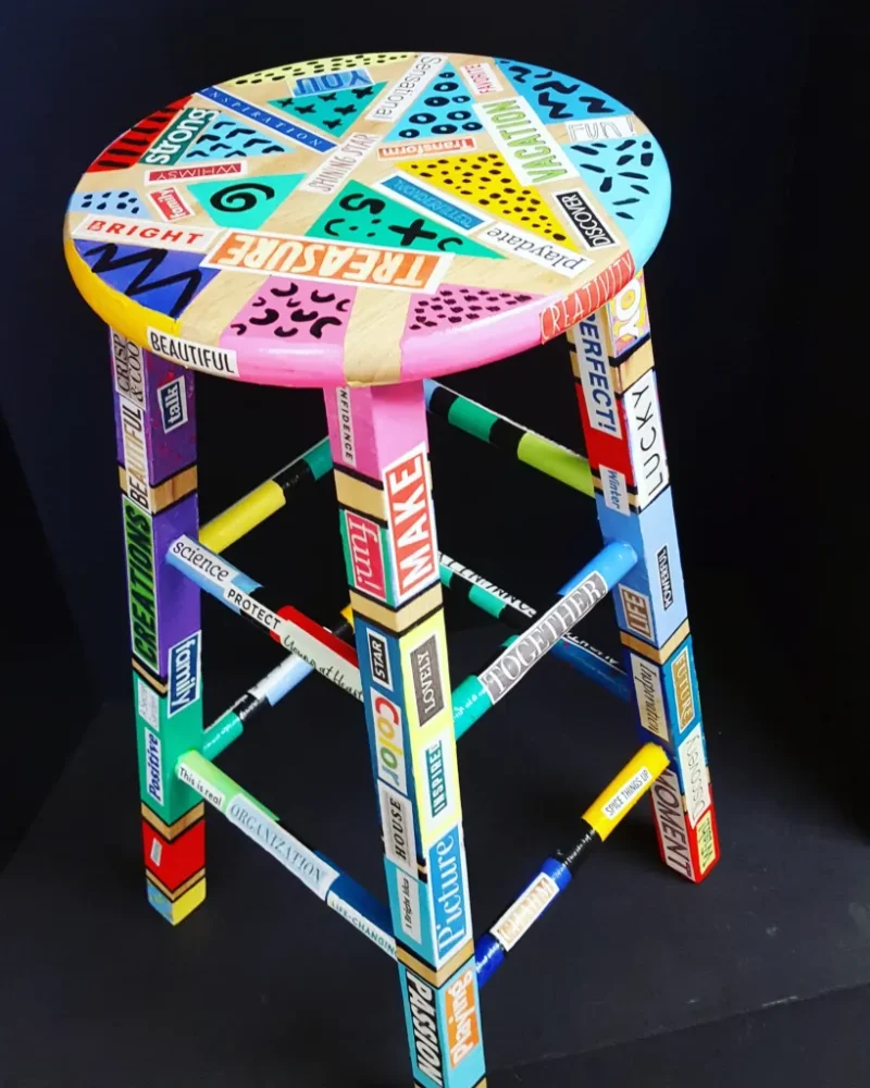 A wooden stool decoupaged with words cut from magazines and Sharpie accents as an example of school auction art projects