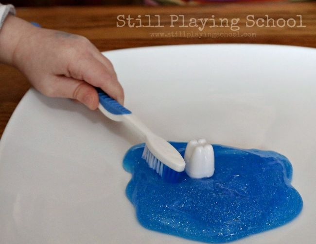 Preschooler playing with toothbrush, plastic tooth, and blue glitter slime