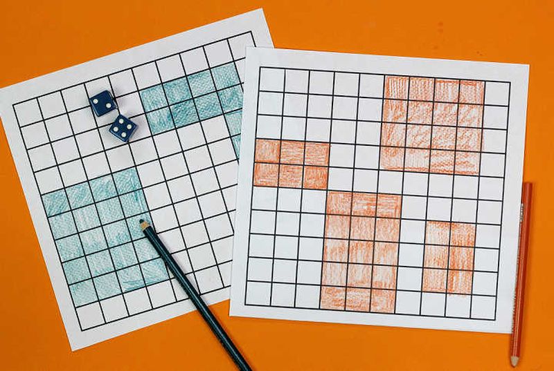 Two pages of grid lines, a pair of dice, and a colored pencil. On each page, several arrays of squares are colored in.