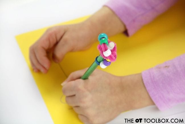 Child writing with a pencil that has a fidget topper made from pipe cleaners and beads
