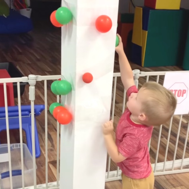 Toddler stretching up to pick a plastic ball off a white column