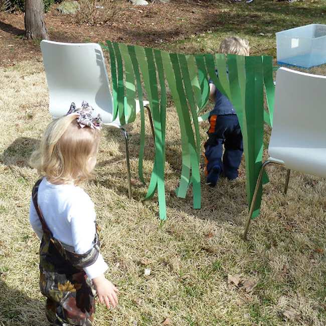 Toddlers climbing through a crepe paper curtain strong across two chairs