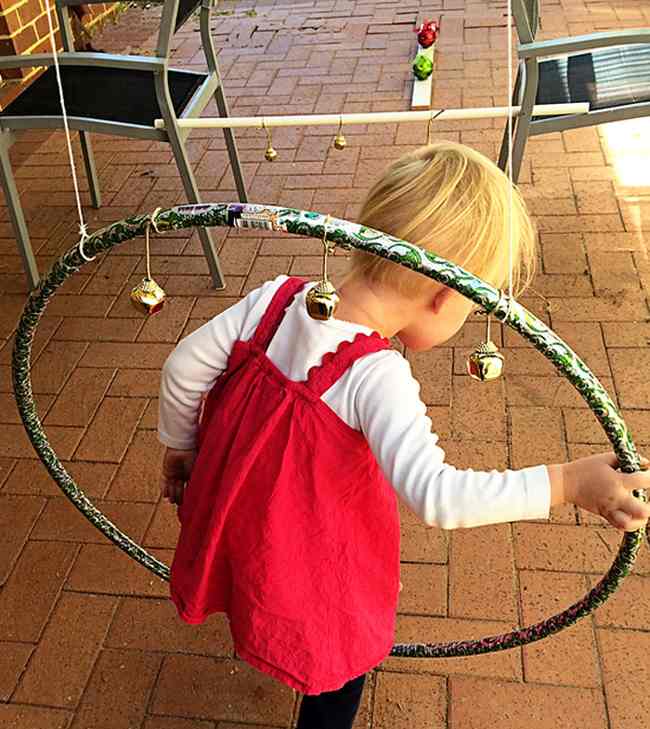 Toddler climbing through a hula hoop with jingle bells attached to it