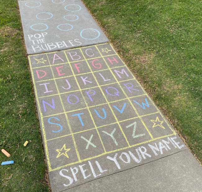 An obstacle course for kids drawn with chalk on a sidewalk, starting with a grid of letters where kids must jump to spell out their name