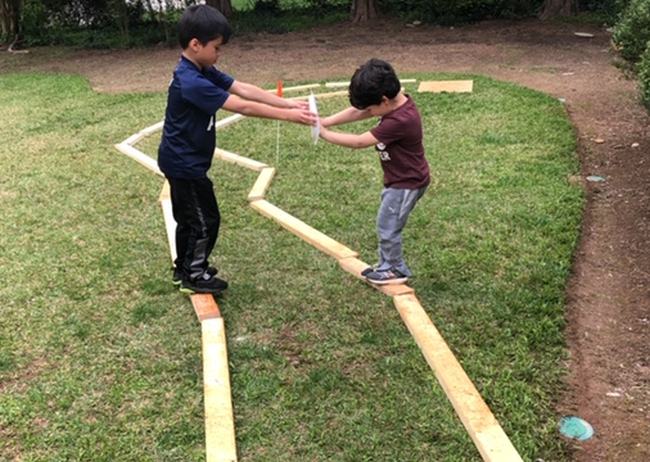 Two kids balancing on narrow beams, holding a plate between them