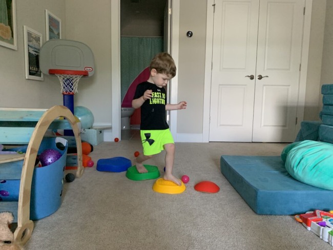 A toddler completing an indoor obstacle course by jumping across colored plastic stepping stones