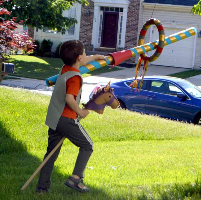 A child riding a hobby horse and stick a cardboard tube through a hoop