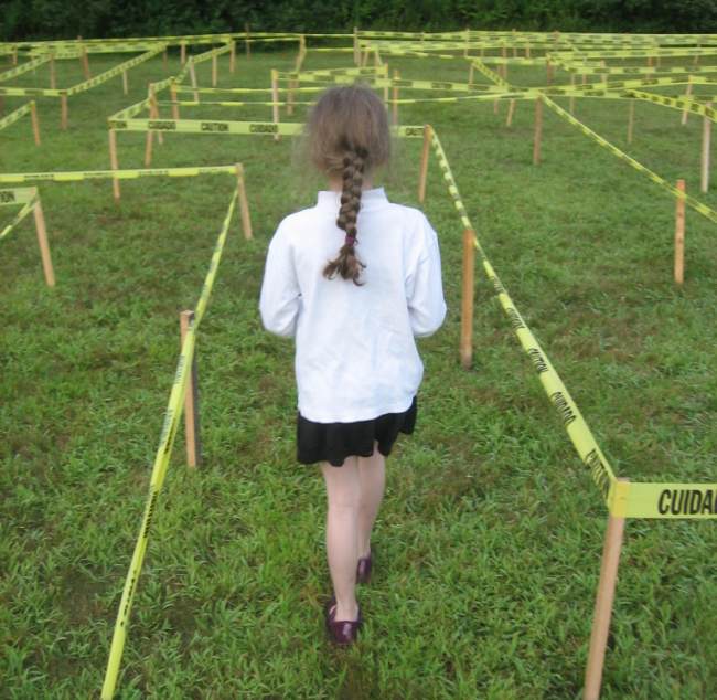 Child standing at the beginning of a maze made of CAUTION tape strung from stakes