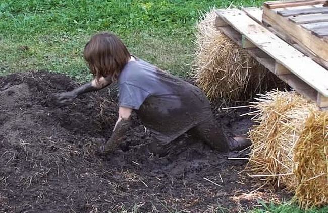 Child crawling through the mud underneath planks laid across hay bales