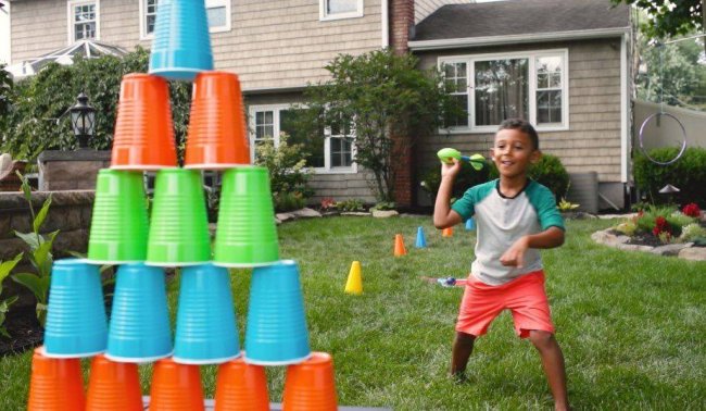 Child throwing a NERF football at a stack of colorful plastic cups