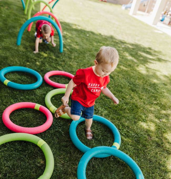 Toddlers climbing under hoops and through circles made of pool noodles, as an example of DIY obstacle courses for kids
