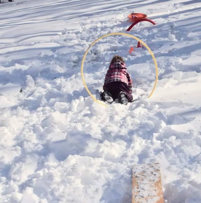 Child climbing through a hoop stuck into a pile or snow, as part of a winter obstacle course for kids