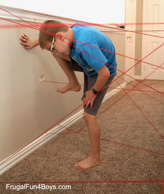 Child climbing over and under strings taped to a wall, trying not to touch them, as an example of DIY obstacle courses for kids