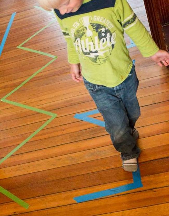 Toddler walking along a masking tape line on a floor, as an example of DIY obstacle courses for kids