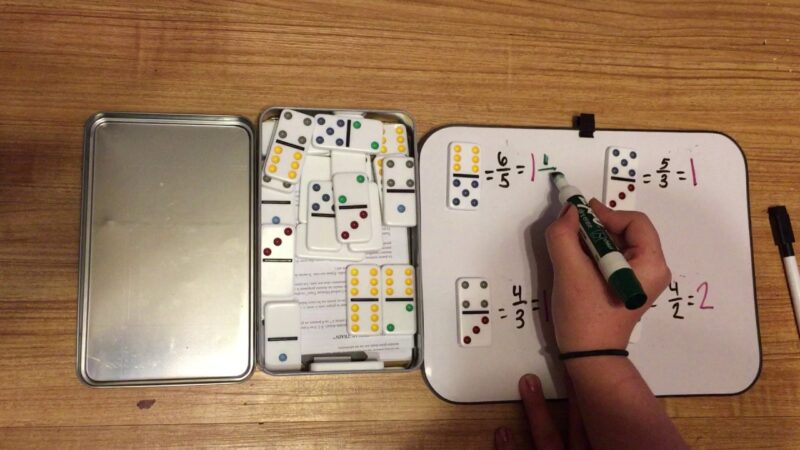 hand writing fraction problems on a magnetic board with dominos for teaching fractions
