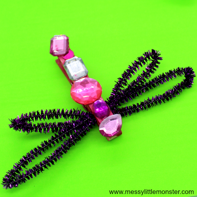 A dragonfly is constructed from a clothespin with gems on it and pipe cleaners for wings (spring crafts for kids)