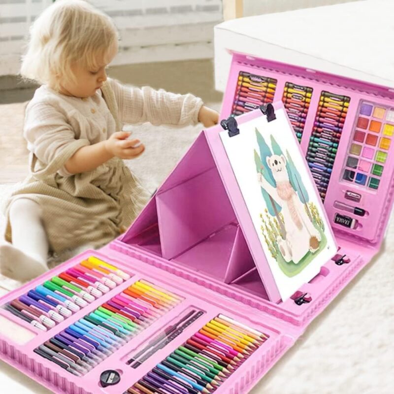 A little girl sits in front of a large pink case that folds open to reveal a variety of art supplies like markers and paint. The center part folds into a tripod easel.