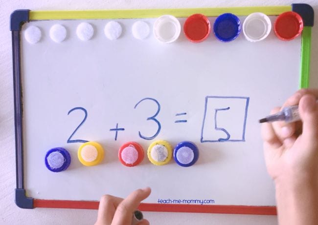 Student using dry erase board and bottlecaps to write 2 + 3 = 5