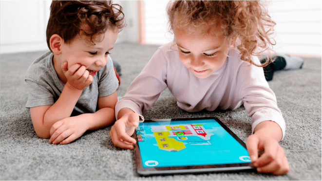 Two preschoolers laying on floor with a tablet that has Duolingo ABC app on the screen