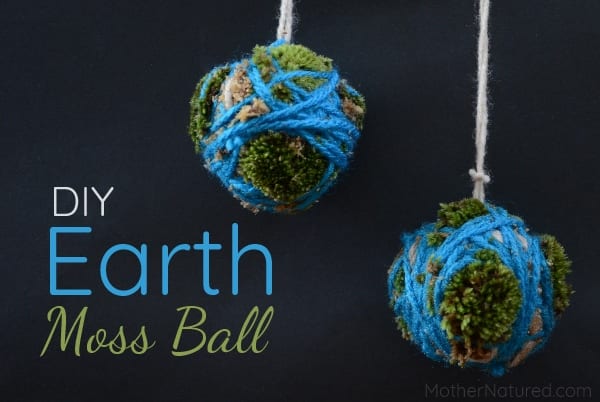 Text on image reads DIY Earth Day Moss Ball. Strings are attached to balls of moss that are wrapped in blue yarn to look like globes.