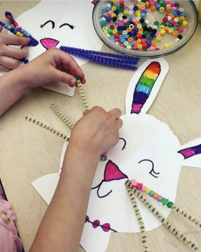 Child stringing beads onto a paper bunny's pipe cleaner whiskers
