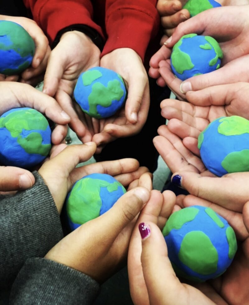 Children's hands holding models of the planet Earth made from clay pressed onto styrofoam balls