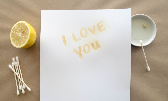 I Love You written in lemon juice on a piece of white paper, with lemon half and cotton swabs