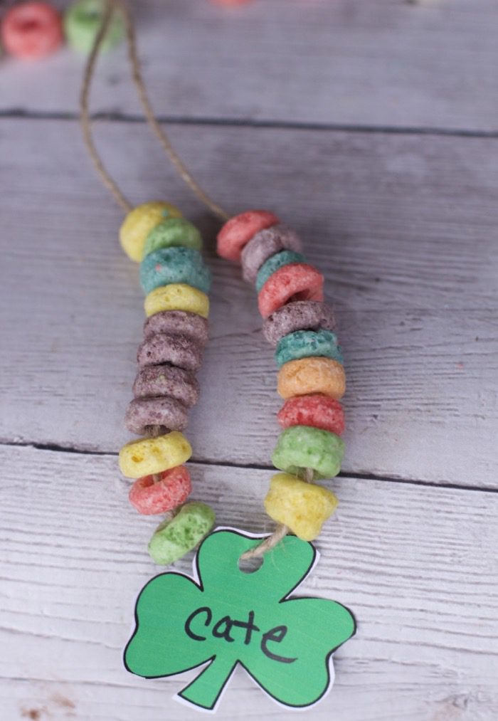 A necklace is constructed of froot loops strung together. A shamrock is at the center with the name Cate. 