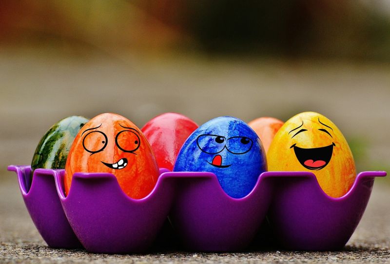 A carton of colorful eggs with faces drawn on them