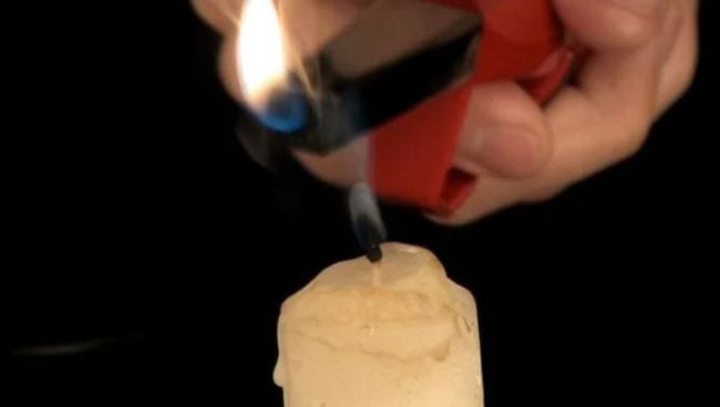 Student's hand holding a lighter over a candle that has just been blown out 