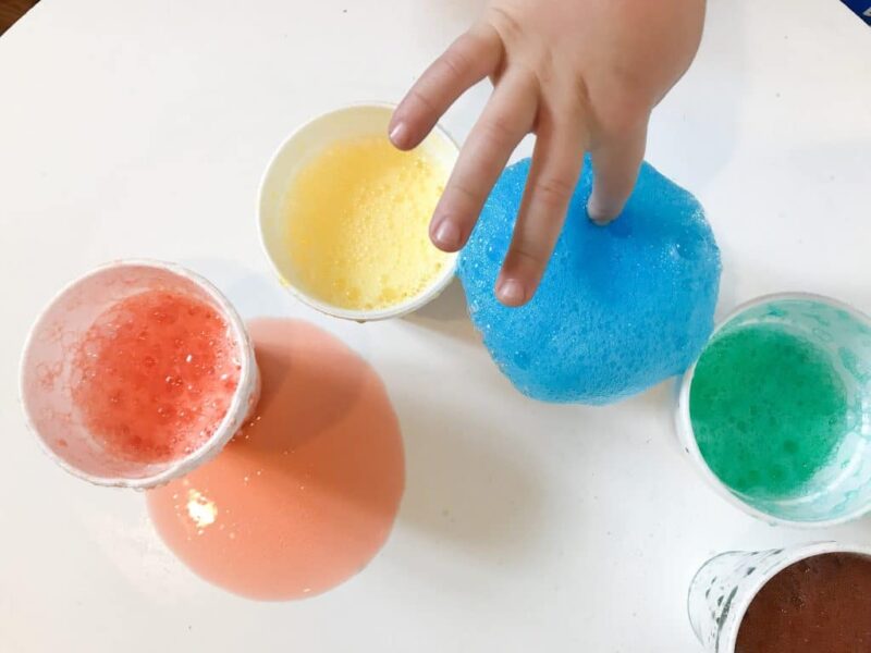 A child pokes his finger into a cup with bubbling blue liquid