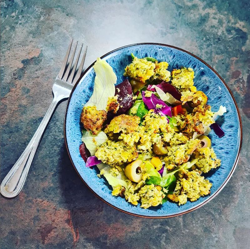 Blue bowl with mixed salad topped with falafel, next to a fork