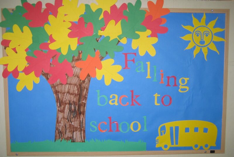 A bulletin board shows a tree with brightly colored fall leaves. A sun and school bus are also present. The words Falling back to school are on the board.