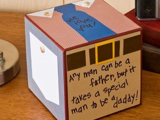 Each side of a cube is decorated. The top looks like the front of a shirt with a tie that reads we love you! The side looks like a pocket square, another side has a belt and says any man can be a father but it takes a special man to be a daddy.