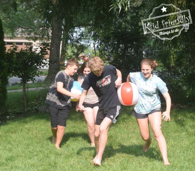 Pairs of students carrying a beach ball without using their hands, trying to win a field day relay race.