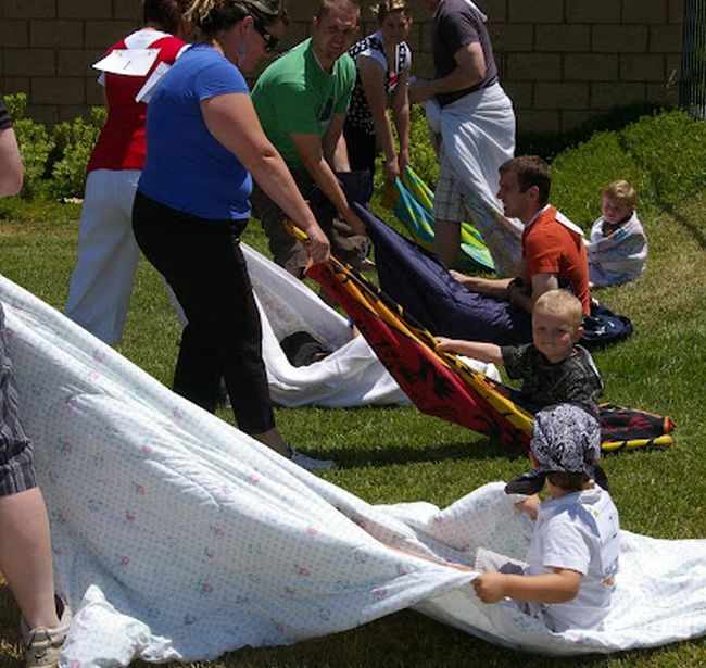 Kids sitting on blankets, while others pull them along in a race (Field Day Games)