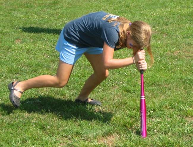 Student with their forehead on the end of a baseball bat, spinning around in a circle as part of field day games.