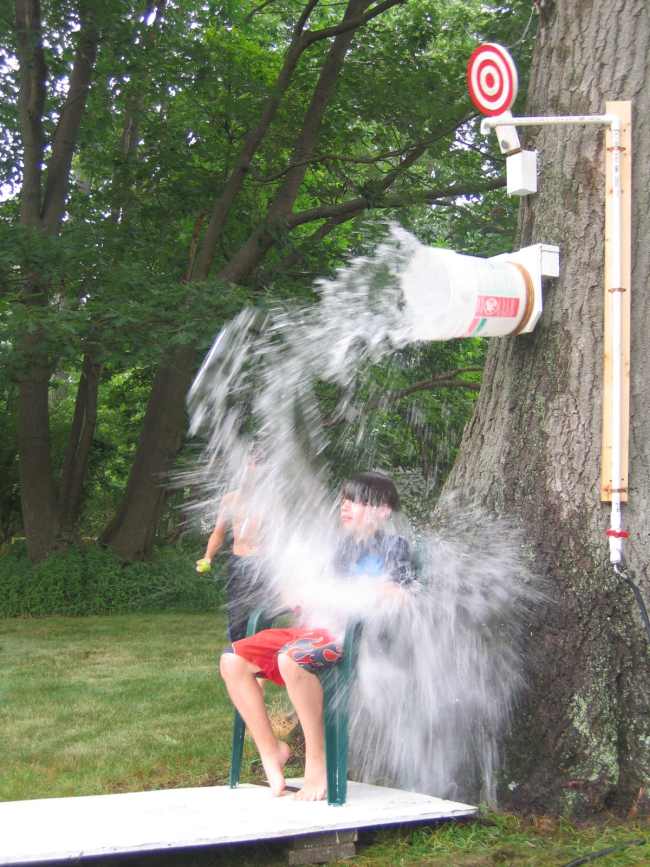 Student sitting under a DIY dunk tank bucket, being doused with water, as they play field day games.
