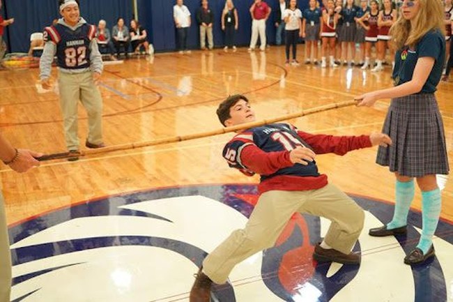 A student bends backwards to limbo under a stick as part of field day games as classmates watch.