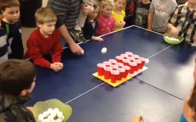 Kids bouncing ping pong balls into plastic cups of water