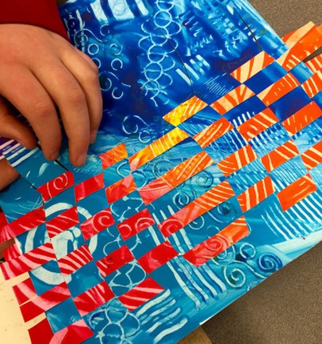 Student weaving together two pages painted in different patterns (Fifth Grade Art)