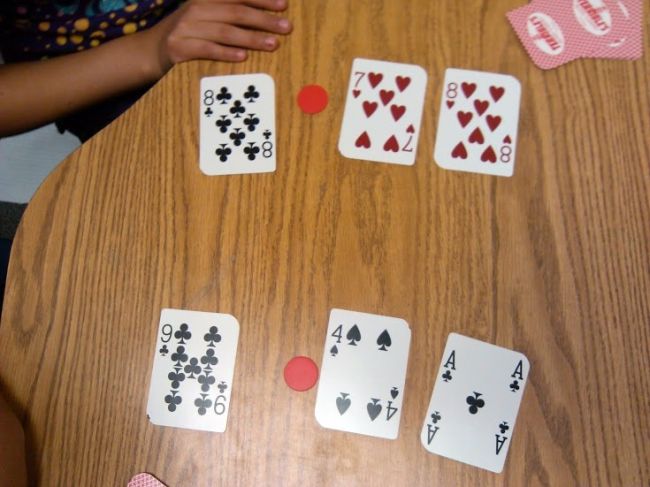 Playing cards laid out face up with red markers to turn them into decimals (Fifth Grade Math Games)