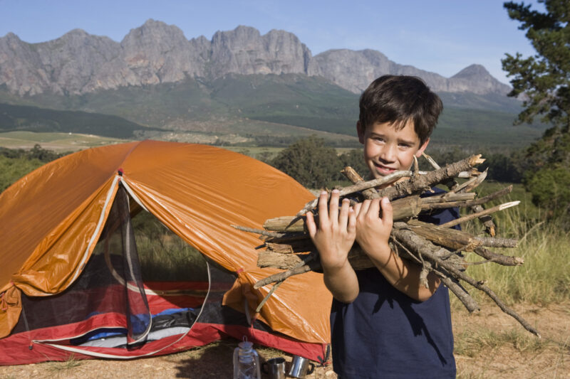 Boy holding firewood in campsite, as an example of camping activities for kids