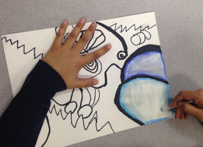 First grade art student adding blue watercolor to a page of scribbles using a cotton swab