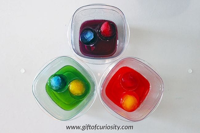 Plastic containers holding colored ice cubes floating in water of different colors