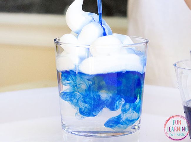 Glass of water with shaving cream on top and blue food coloring dropping down