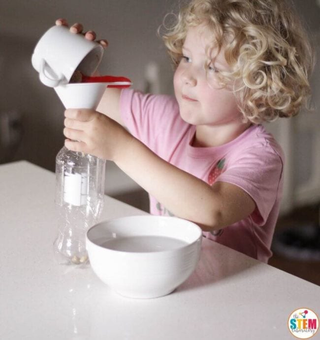 Young student pouring yeast through a funnel into a plastic bottle