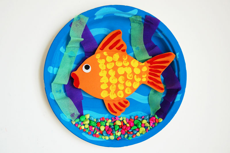 A blue bowl has a painted fish in it with colorful gravel (first grade art)