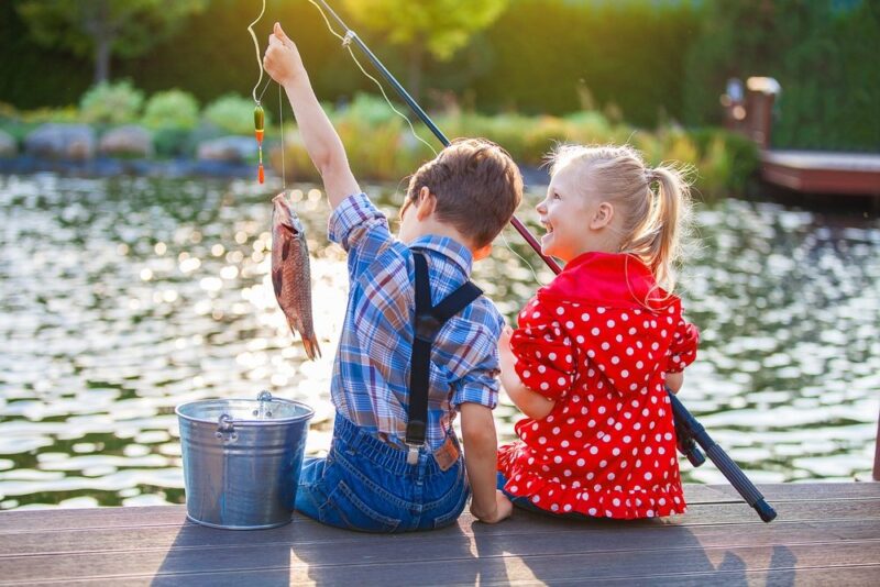 Two kids sitting on dock fishing, as an example of camping activities for kids
