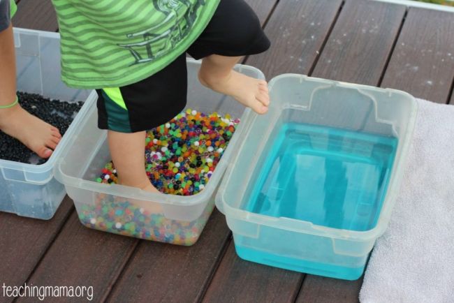 Toddlers walking through plastic tubs filled with different substances to teach the five senses 